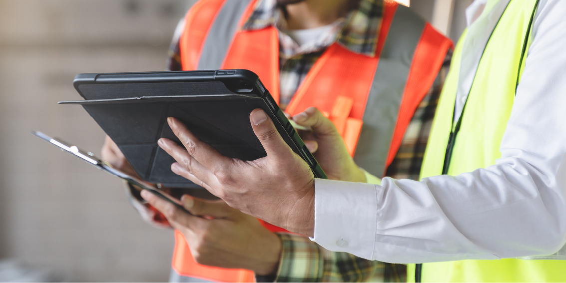 This image depicts two people in fluorescent vests looking at a PDA together. 