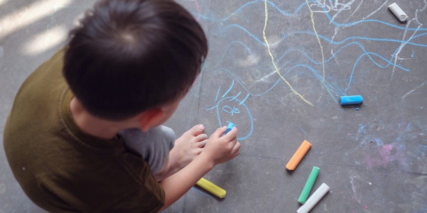 image of a young child playing with drawing with coloured chalk sticks