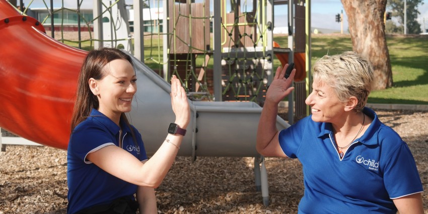 Image of two women in a children's playground high fiving each other