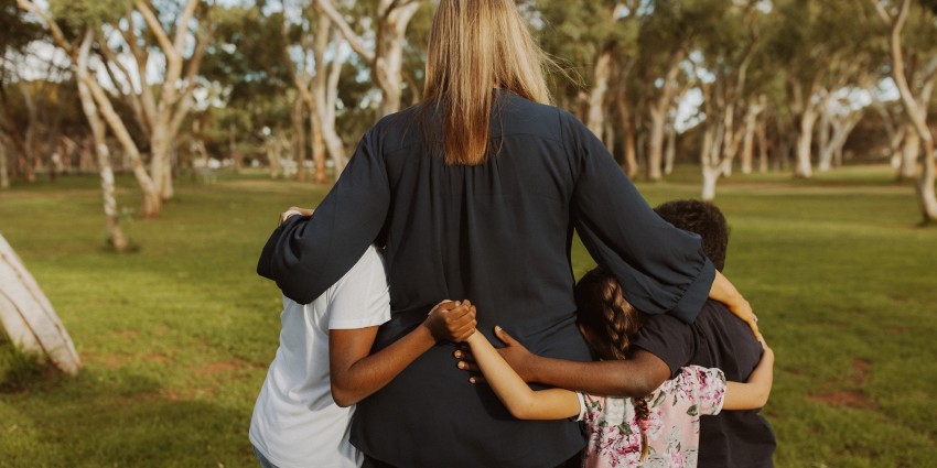 photo of a woman with her arms around three young children on a grass field