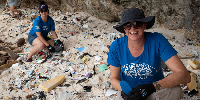 ladies in blue tshirts, hats and sunglasses collecting rubbish off beach