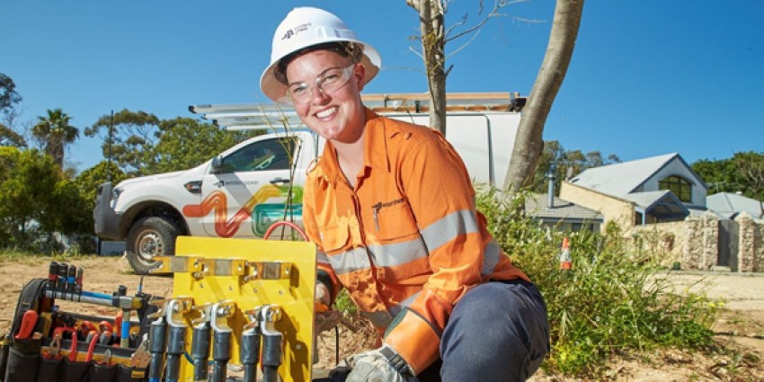 Female electrician working with tools in an outdoor park wearing hi vis uniform and a hard hat.