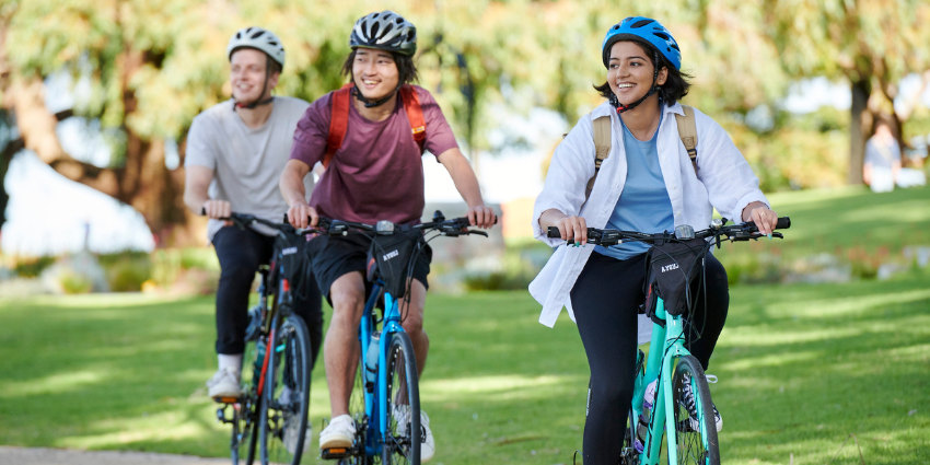 green grass in the background of three people cycling together smiling and looking to the side