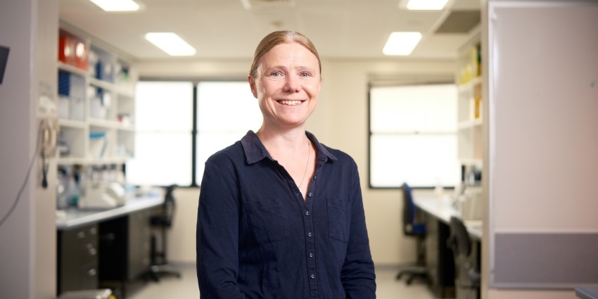 women in navy blouse smiling with office lab behind her