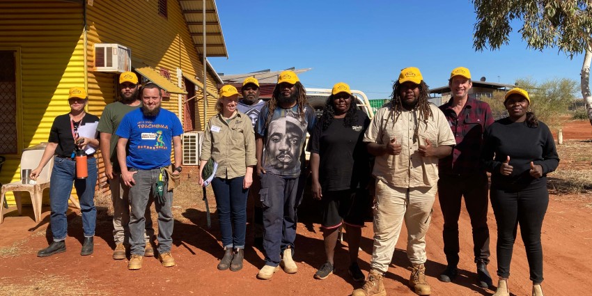 A group photo of people standing in front of a yellow house in a remote town.