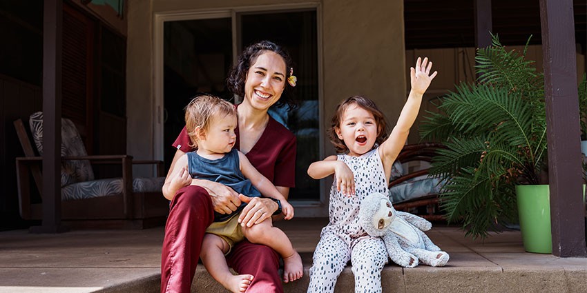 A mother with two young children sitting on their patio, smiling.