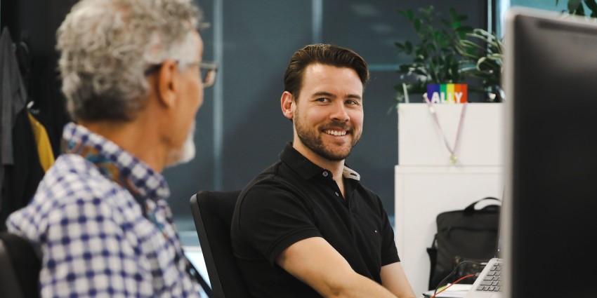 A photo of 2 smiling people sitting at their desk