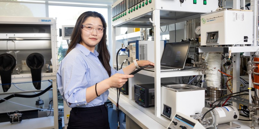 young asian girl working in a scientific lab, wearing blue dress shirt and black trousers and safety glasses