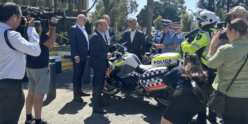 Public officials and the media grouped around a parked police motorcycle