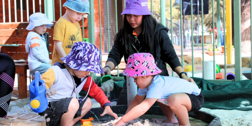 Photo of a early childhood education and care playground with children and a female educator playing together