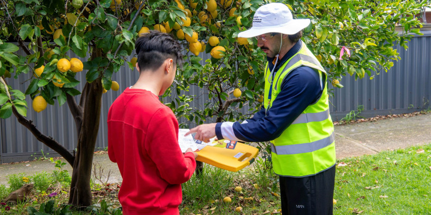 A man in a tabbard with a clipboard talking to another man near a lemon tree.