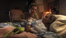  A woman and child lying together in a hospital bed, holding hands, surrounded by medical equipment.