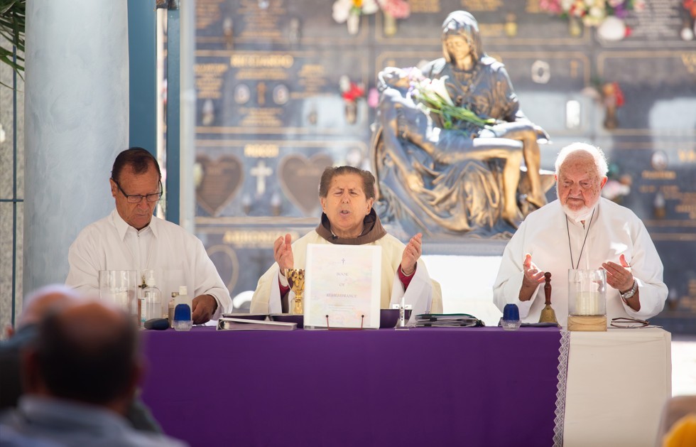 three men wearing robes perform a Catholic prayer