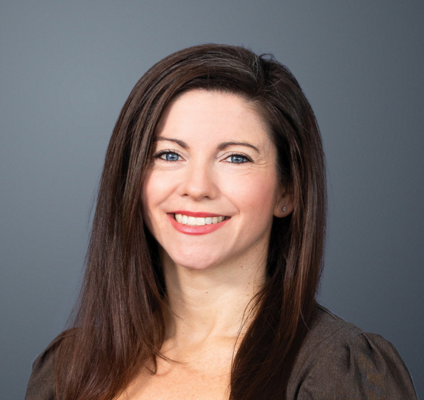 woman with thick dark hair in a side part wearing brown blouse smiling at camera