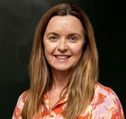 middle ages woman with light brown hair in orange and pink floral blouse smiling