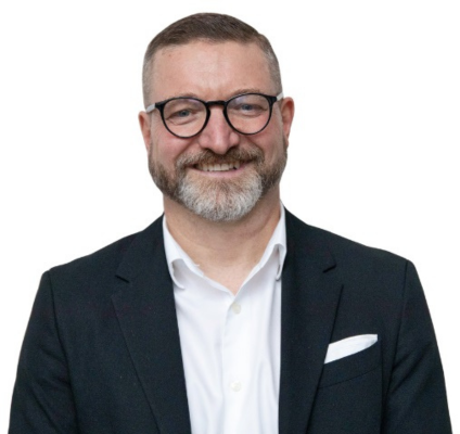 older white man with light brown hair, brown spectacles and a grey beard wearing white dress shirt and black blazer and smiling